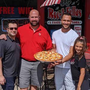 People posing for a photo while holding a pizza